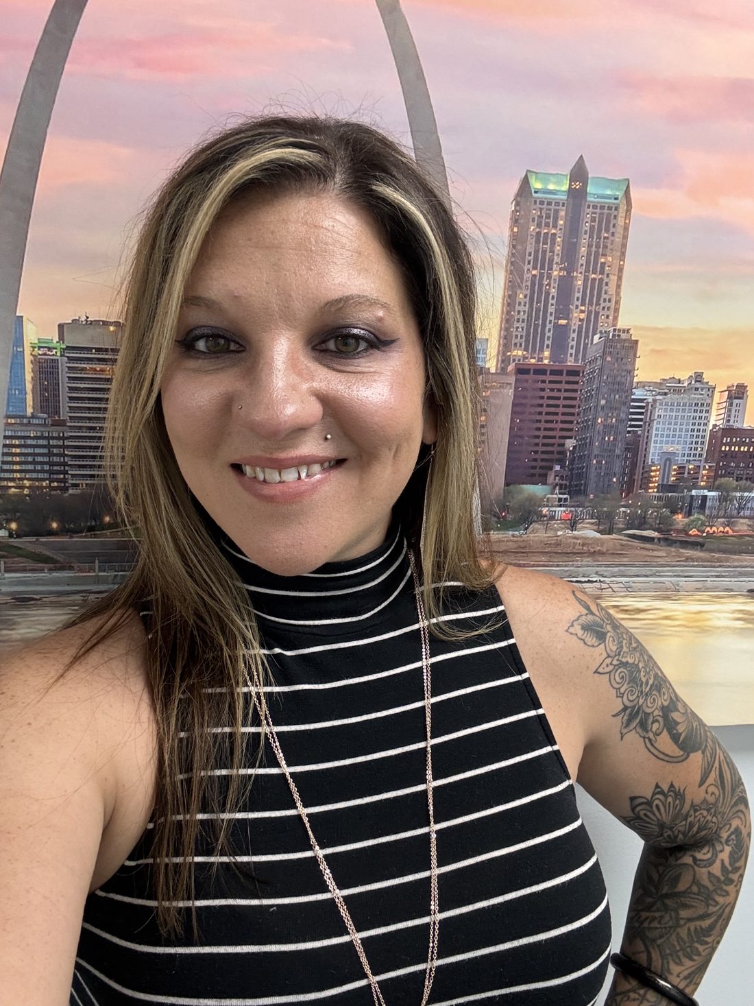 Joanna in a black and white striped top, with the St. Louis skyline and Gateway Arch behind her
